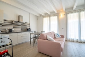 Une cuisine moderne avec des meubles blancs, un coin repas comprenant une table et des chaises, et un salon avec un canapé et des rideaux.