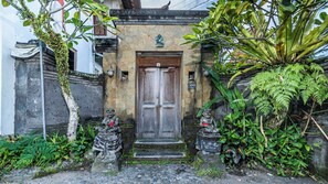 A traditional wooden door with a stone wall, two stone statues, and lush greenery. - Pondok Loris (Ubud)
