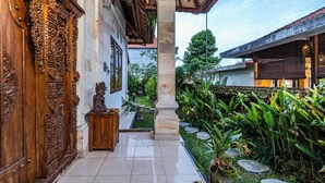 A traditional wooden door with intricate carvings, a stone pillar, and a garden with tropical plants. - Pondok Loris (Ubud)