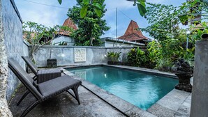A swimming pool with a stone wall, a concrete bench, and tropical plants. - Pondok Loris (Ubud)
