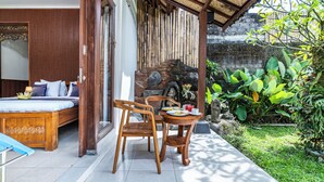 A room with a bed, a wooden chair, a dining table with plates and a drink, and a stone wall with plants. - Pondok Loris (Ubud)