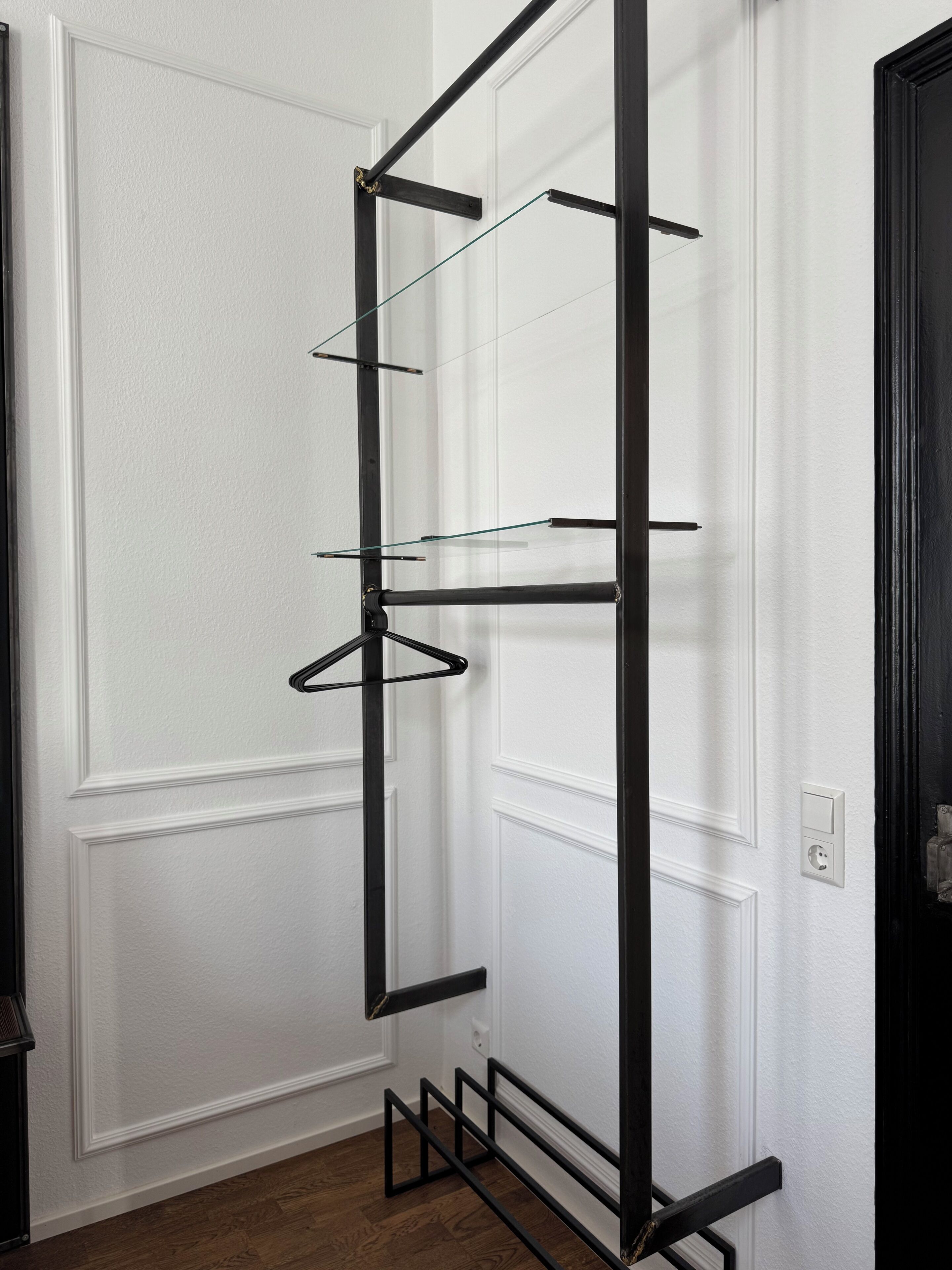 A black metal shelf unit with multiple shelves against a white door.