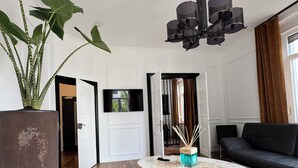 A modern living room with a round marble coffee table, a black leather sofa, a large potted plant, and a unique ceiling light fixture. - HLH - Luxus Familiensuite mit Terrasse (Freiburg im Breisgau)