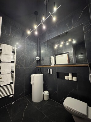 Une salle de bain moderne avec un mur en marbre noir, un lavabo blanc, des toilettes et un porte-serviettes.