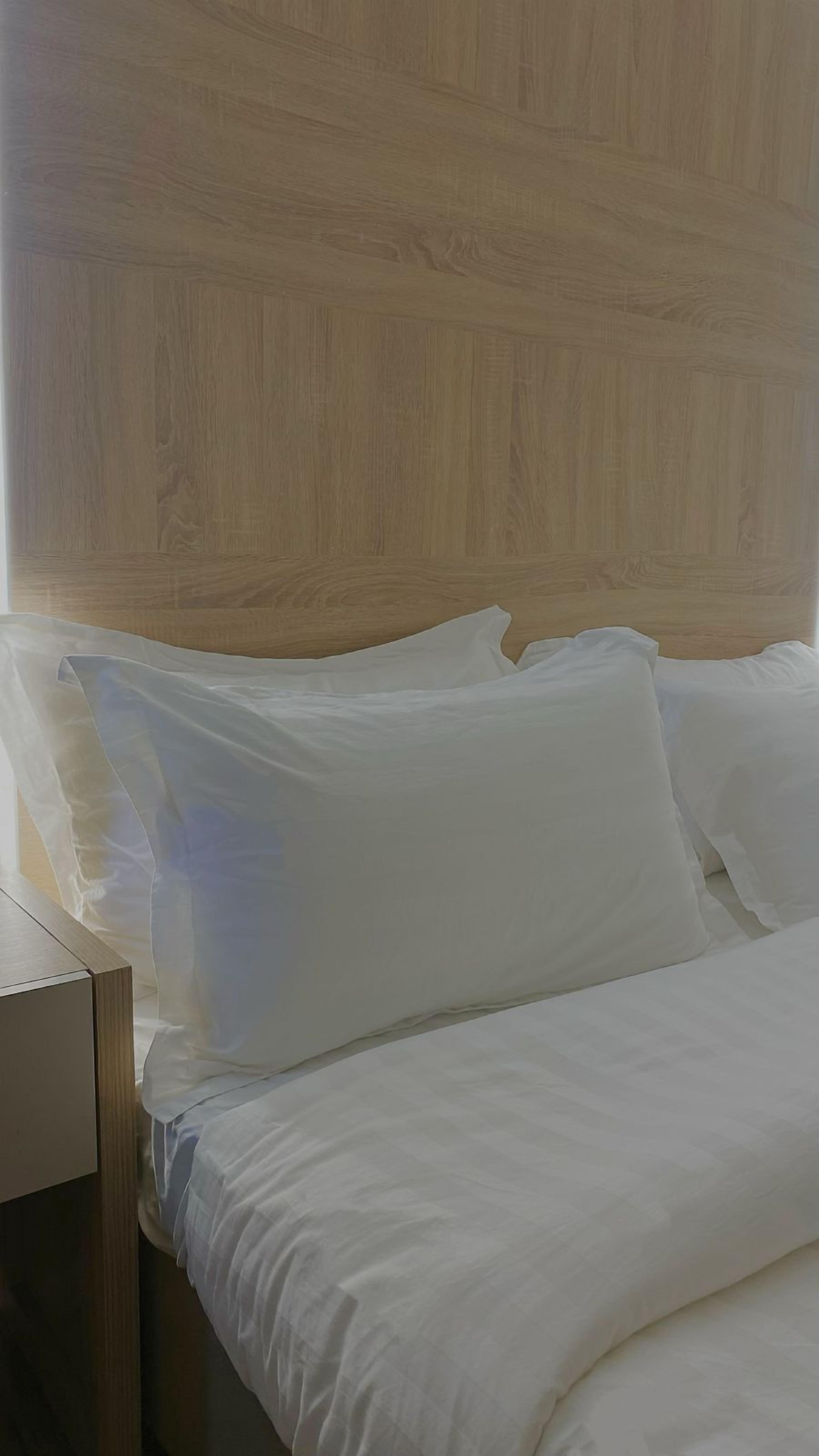A neatly made bed with white linens in a room with a wooden headboard.