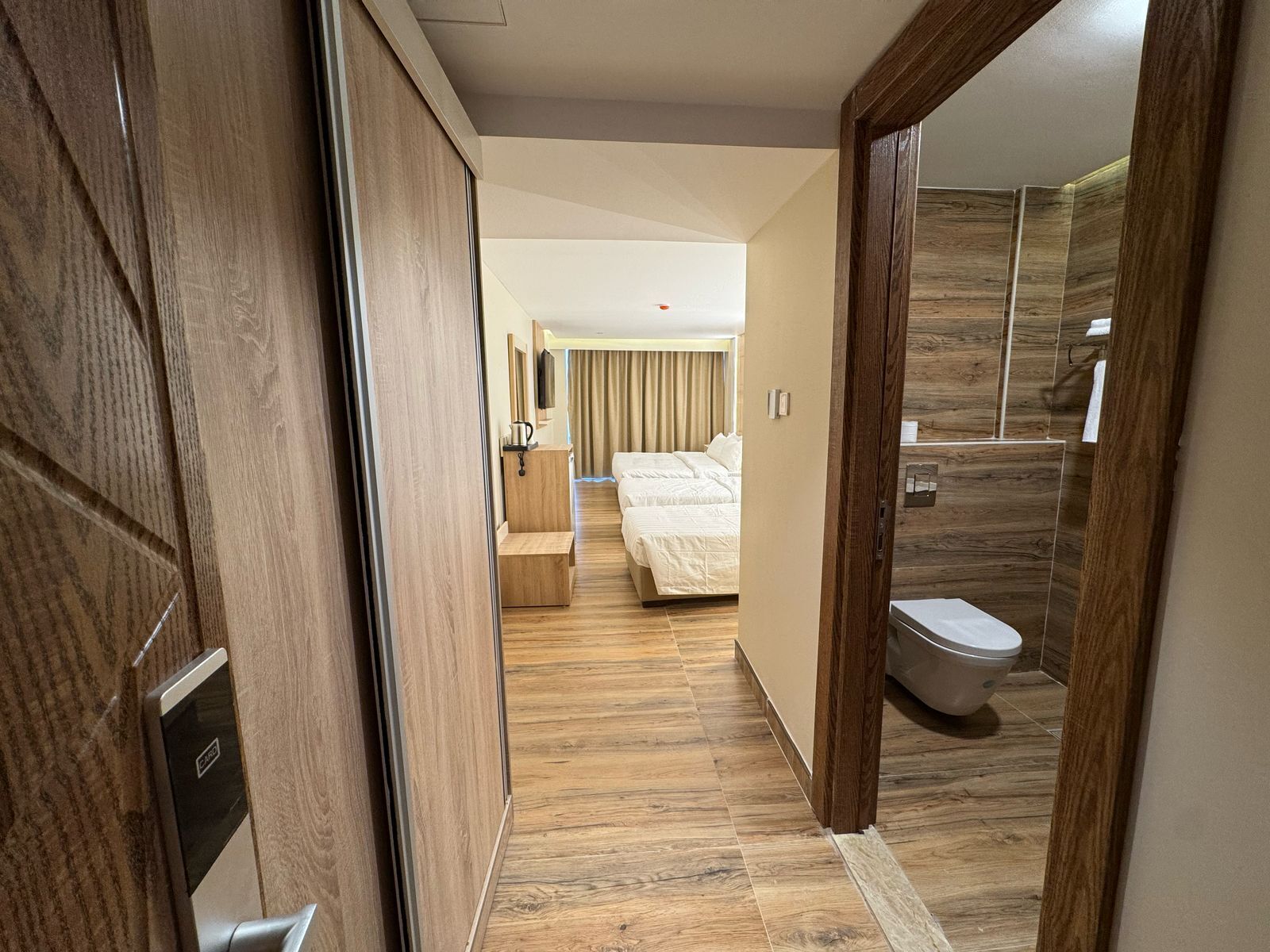 Hotellihuone, jossa on puulattia, sänky, yöpöytä, peili ja wc.