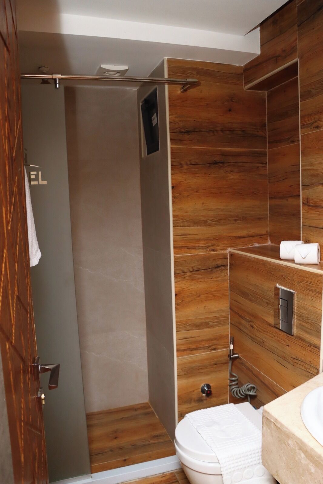 A modern bathroom with wooden paneling, a toilet, a shower, and a towel rack.
