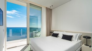 Ein modernes Hotelzimmer mit einem großen Bett, einem Nachttisch, einer Lampe und Meerblick durch eine Schiebetür.