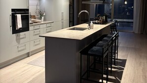A modern kitchen with a central island, bar stools, and a view of the outdoors.
