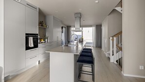A modern kitchen with white cabinetry, a central island with bar stools, and a view to the living area.