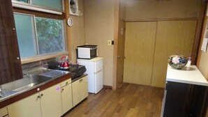 Cozinha compacta com pia, micro-ondas e geladeira. Uma porta de madeira dá acesso a outro quarto.