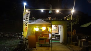 Uma pequena área de refeições ao ar livre com uma bicicleta estacionada ao lado, mesa e cadeiras, e uma estrutura em forma de tenda com luzes.