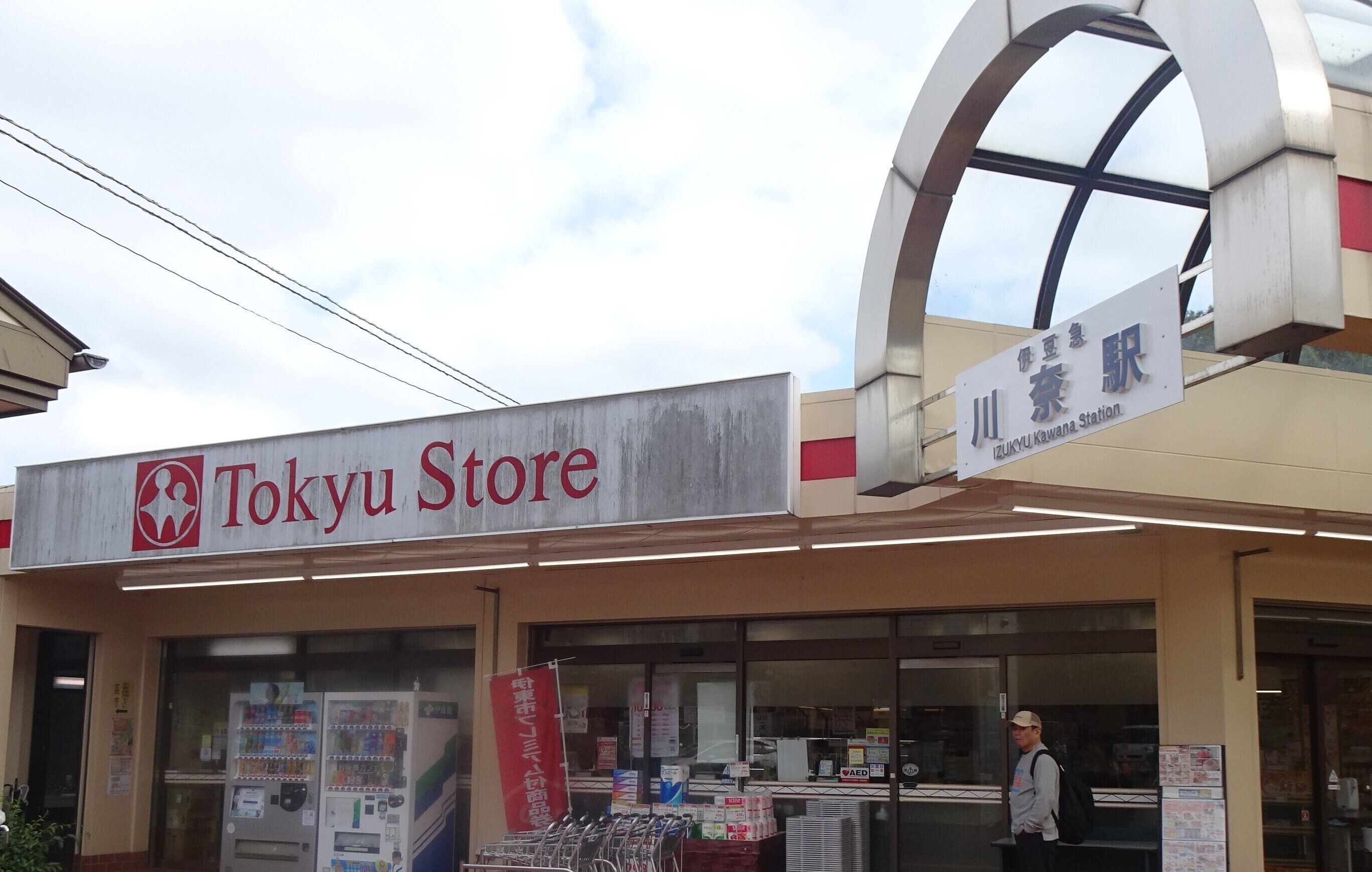 Un negozio a Tokyo con distributori automatici all'esterno e un cartello che indica la stazione di Izukyu Kawana.