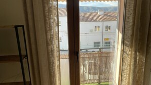 Una habitación con puerta corrediza de vidrio que da a un balcón, suelo de madera y una escalera metálica contra la pared.