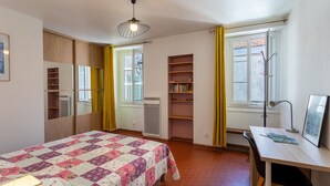 A bedroom with a bed, a desk, a chair, a radiator, a window with curtains, and a bookshelf. - VUE ROSSETTI AP4465 by Riviera Holiday Homes (Niza)