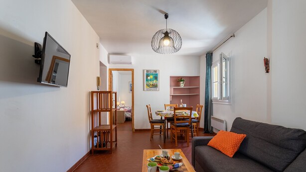 A living room with a sofa, a coffee table with a tray of food, a dining area with a table and chairs, and a TV mounted on the wall. - VUE ROSSETTI AP4465 by Riviera Holiday Homes (Niza)