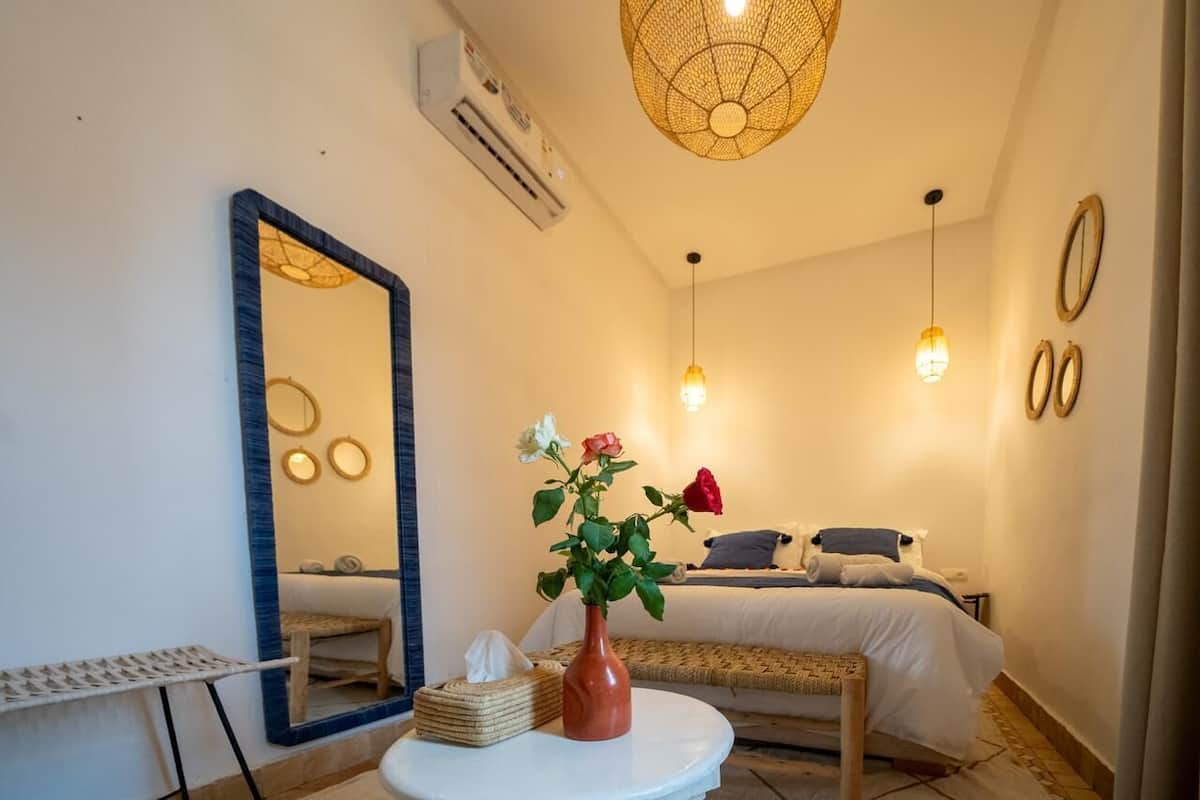 A bedroom with a bed, bedside table, mirror, and a vase with flowers.
