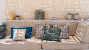 Ein beiges Sofa mit gestreiften und einfarbigen Kissen, eine dekorative Vase und Topfpflanzen vor einer Steinwand.