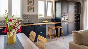 Eine moderne Küche mit dunklen Schränken, einer Holzarbeitsplatte und einem eingebauten Backofen. Zwei Fenster sorgen für natürliches Licht, und auf dem Esstisch steht eine Vase mit Blumen.