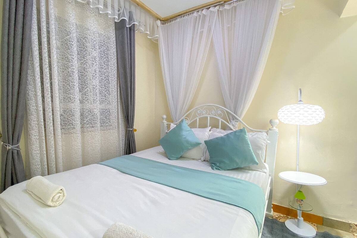 A neatly made bed with a white headboard, two teal pillows, and a white blanket.