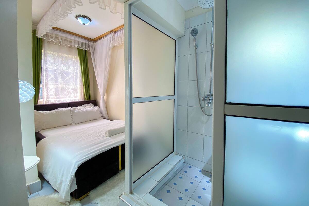 A bedroom with a bed, a shower, and a window with curtains.