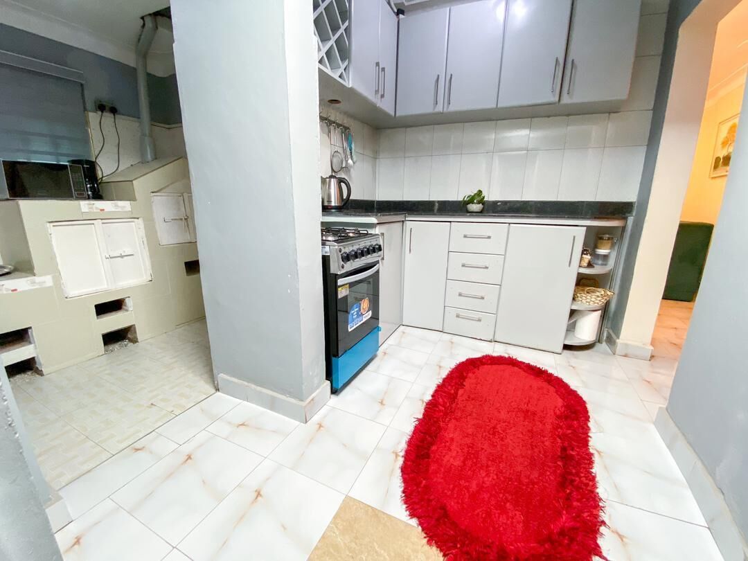 Une cuisine avec des meubles blancs, un fourneau et un tapis rouge.