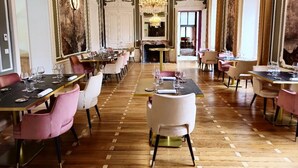 Een ruime eetruimte met meerdere tafels en stoelen, versierde wanddecoraties en een kroonluchter.