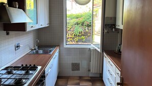 Een kleine keuken met een gasfornuis, gootsteen en een raam met uitzicht op een tuin.