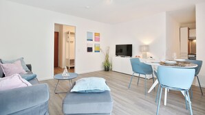 A modern living room with a sofa, ottoman, and a dining area with chairs and a table. - Vacation home Bergstraße 62 Apartment 5 Tide am Park (Timmendorfer Strand)