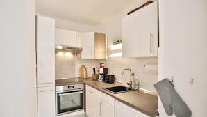 A modern kitchen with white cabinetry, stainless steel appliances, and a grey oven. - Vacation home Bergstraße 62 Apartment 5 Tide am Park (Timmendorfer Strand)