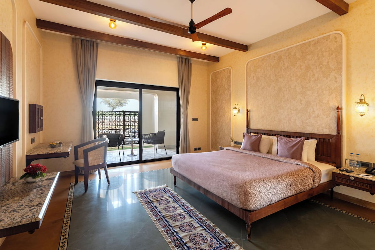 A spacious bedroom with a large bed, a desk, and a chair. There is a sliding glass door leading to a balcony.