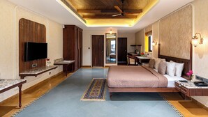A spacious bedroom with a large bed, a flat-screen TV, wooden headboard, and a ceiling fan. - Chavri Resort – A Luxury Stay In Jawai (Bali)
