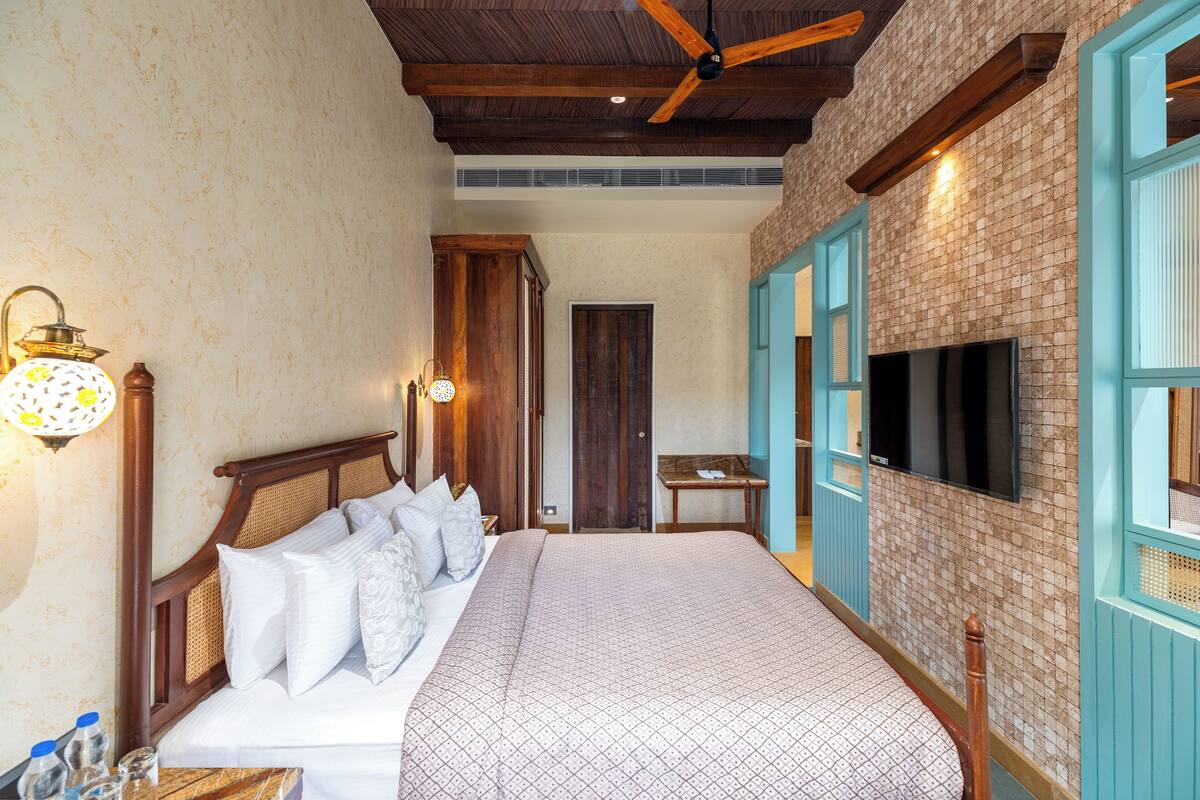 A hotel room with a large bed, wooden headboard, a flat-screen TV mounted on the wall, and a ceiling fan.