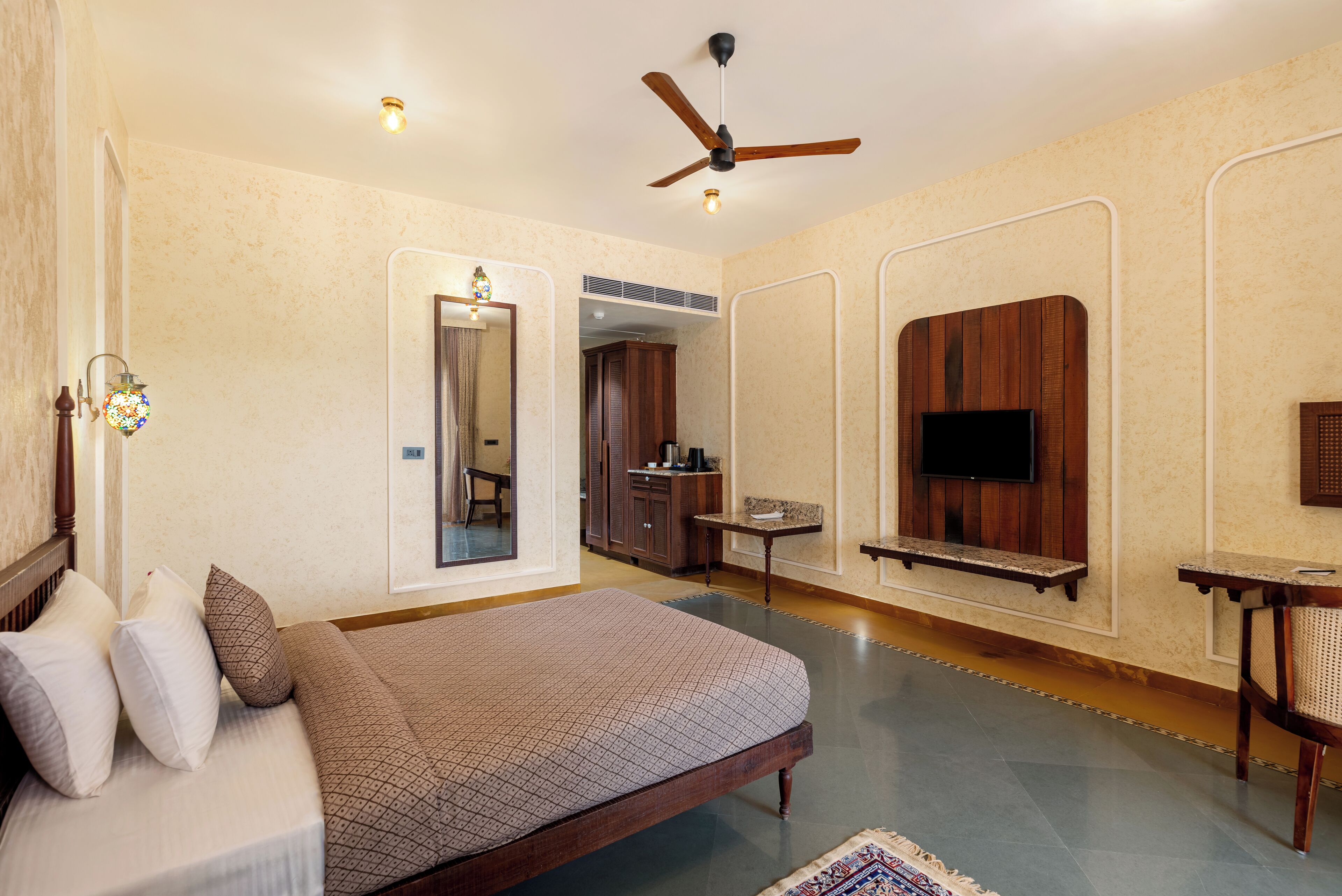 A bedroom with a bed, a ceiling fan, a TV mounted on the wall, and a small table.