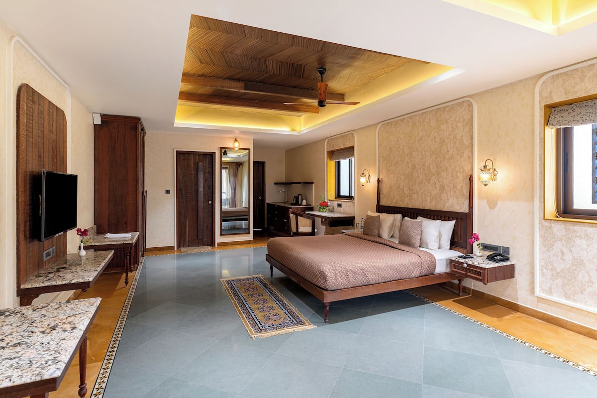 A spacious hotel room with a large bed, a flat-screen TV, a desk, and a seating area.