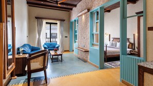 A hotel room with a large bed, a sitting area with a sofa and chairs, and a view of the city through the window. - Chavri Resort – A Luxury Stay In Jawai (Bali)