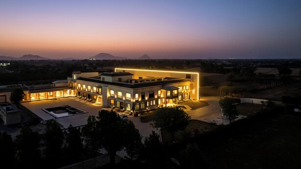 A modern hotel with multiple buildings connected by a central structure, surrounded by open land and distant mountains. - Chavri Resort – A Luxury Stay In Jawai (Bali)