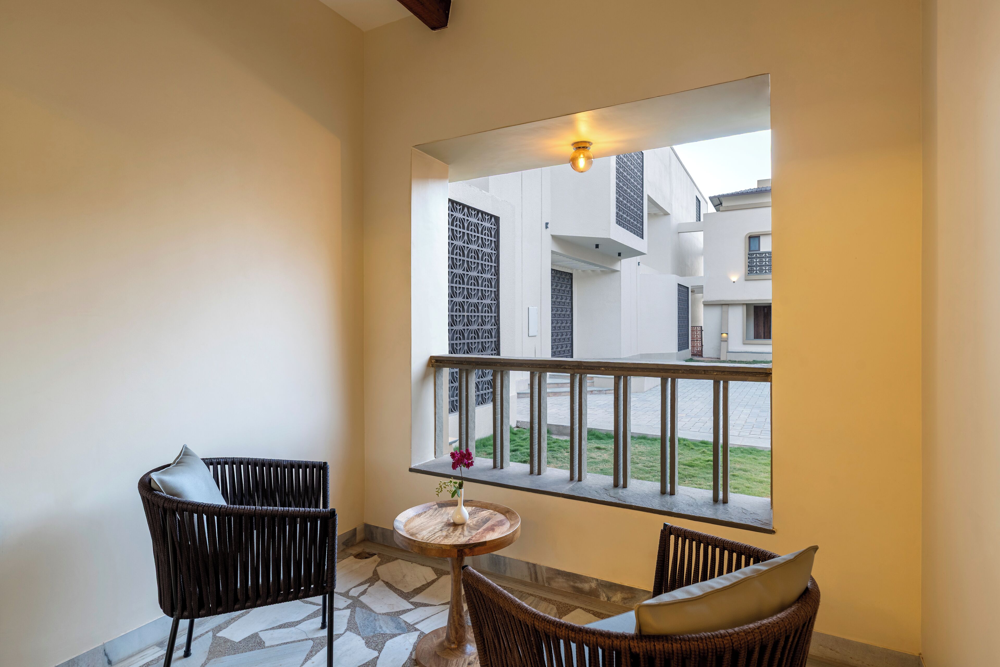 A balcony with wicker chairs, a small round table with a vase, and a view of a building with a balcony railing.