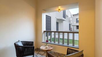 A balcony with wicker chairs, a small round table with a vase, and a view of a building with a balcony railing.