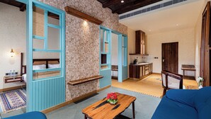 A room with a blue sofa, a wooden table with a flower, and a kitchen area in the background. - Chavri Resort – A Luxury Stay In Jawai (Bali)