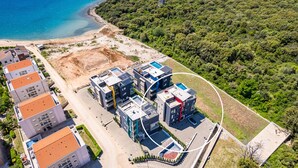 Luchtbeeld van een kustgebied met woonwijken, moderne gebouwen, een strand en dicht bos.