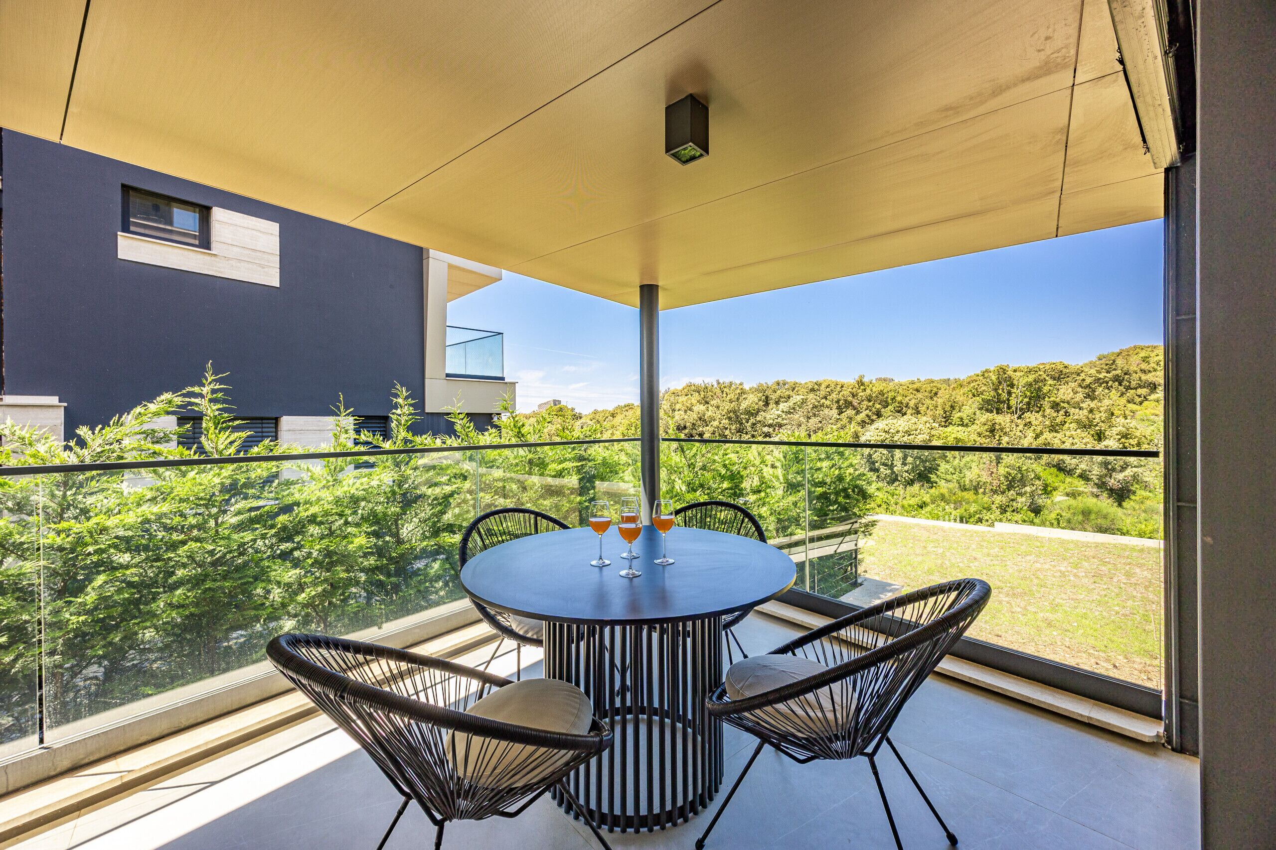 A balcony with a round table and four chairs, overlooking a lush green landscape.