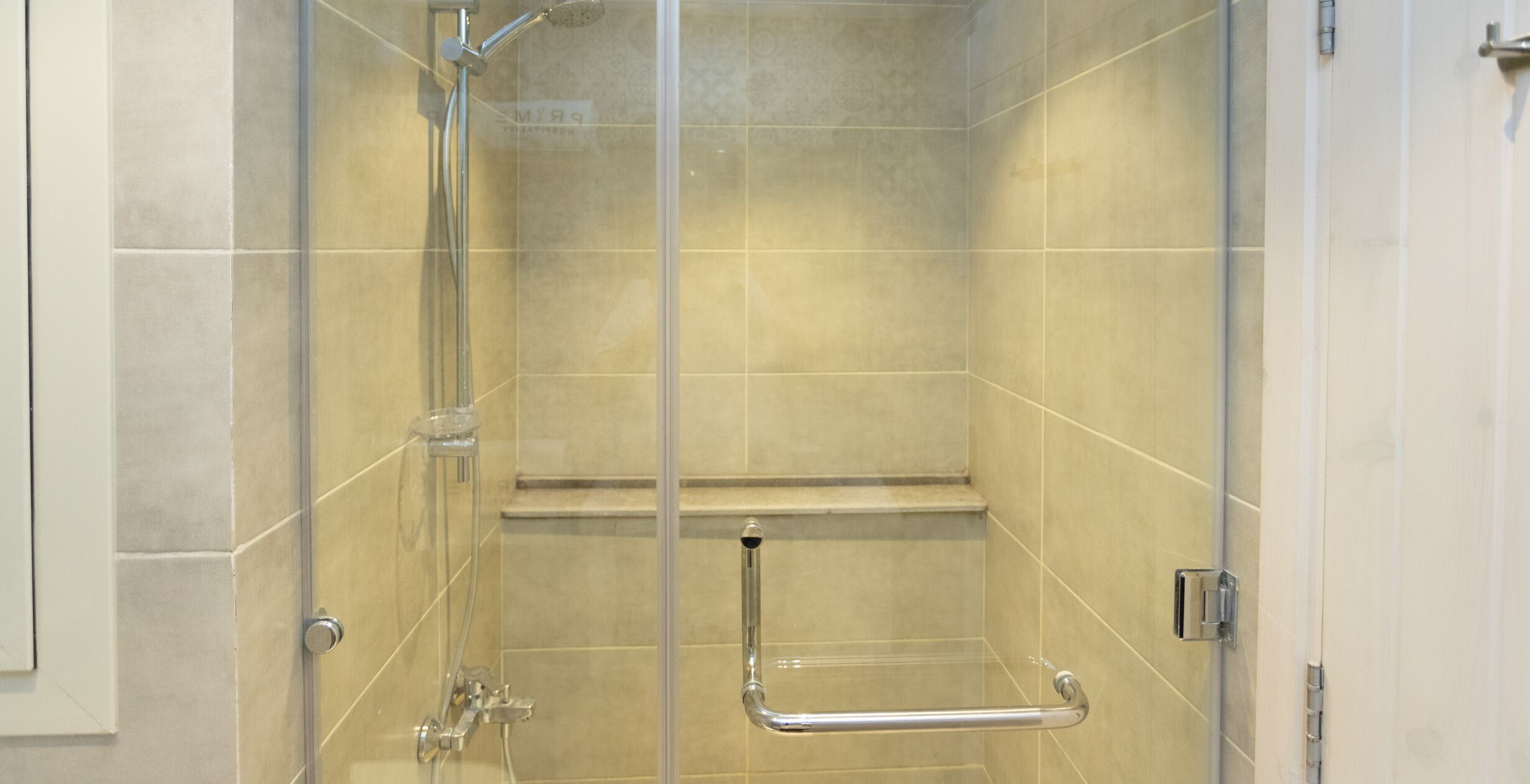 A glass-enclosed shower stall with a handrail, a showerhead, and a control panel.