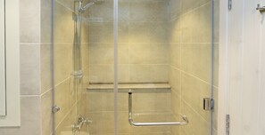 A glass-enclosed shower stall with a handrail, a showerhead, and a control panel.