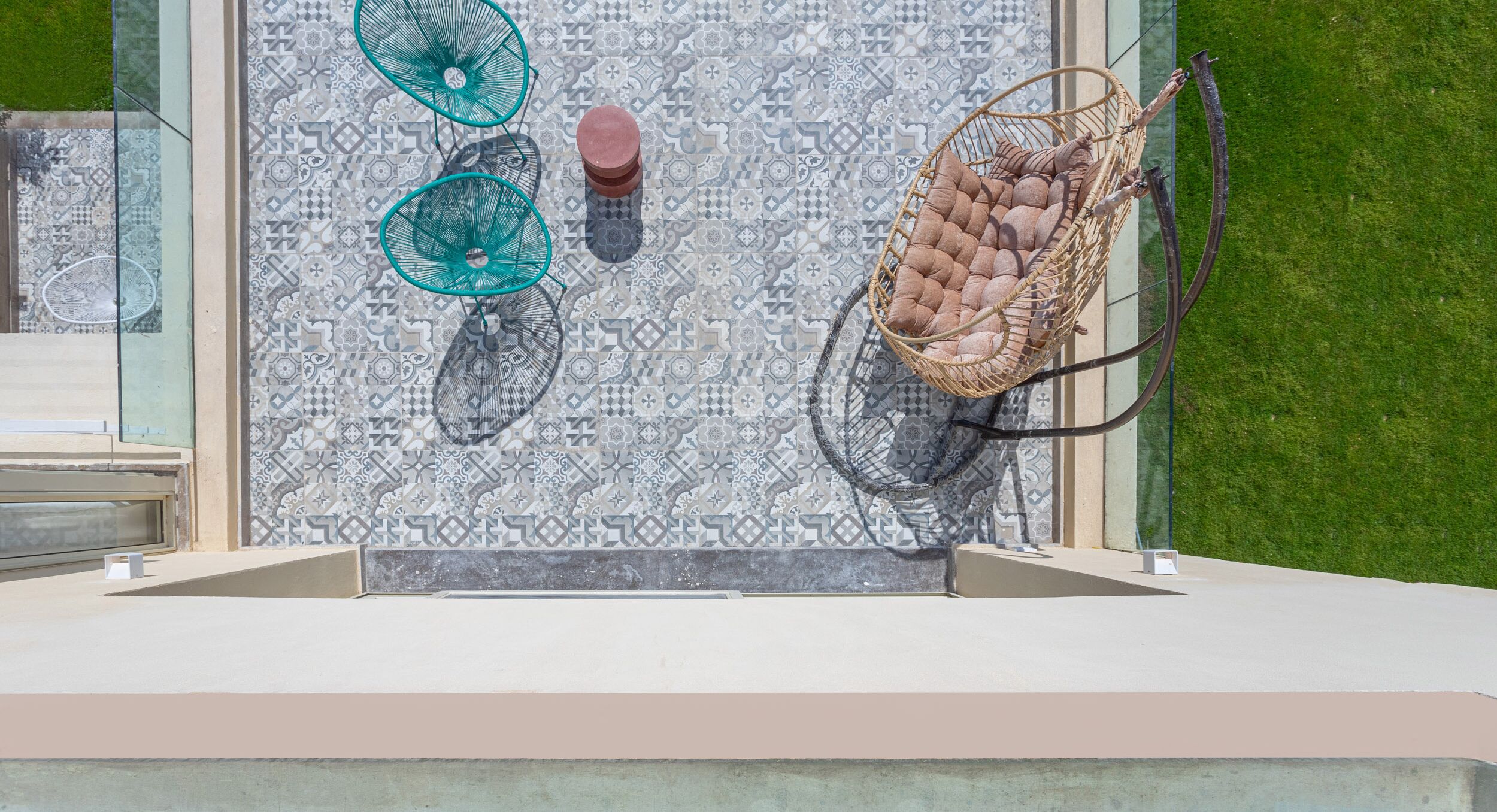 A balcony with a patterned tile wall, a wicker swing chair, and two green fans.