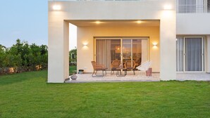 Een modern terras buiten met een tafel, stoelen, een grote schuifpui en een verzorgd gazon.