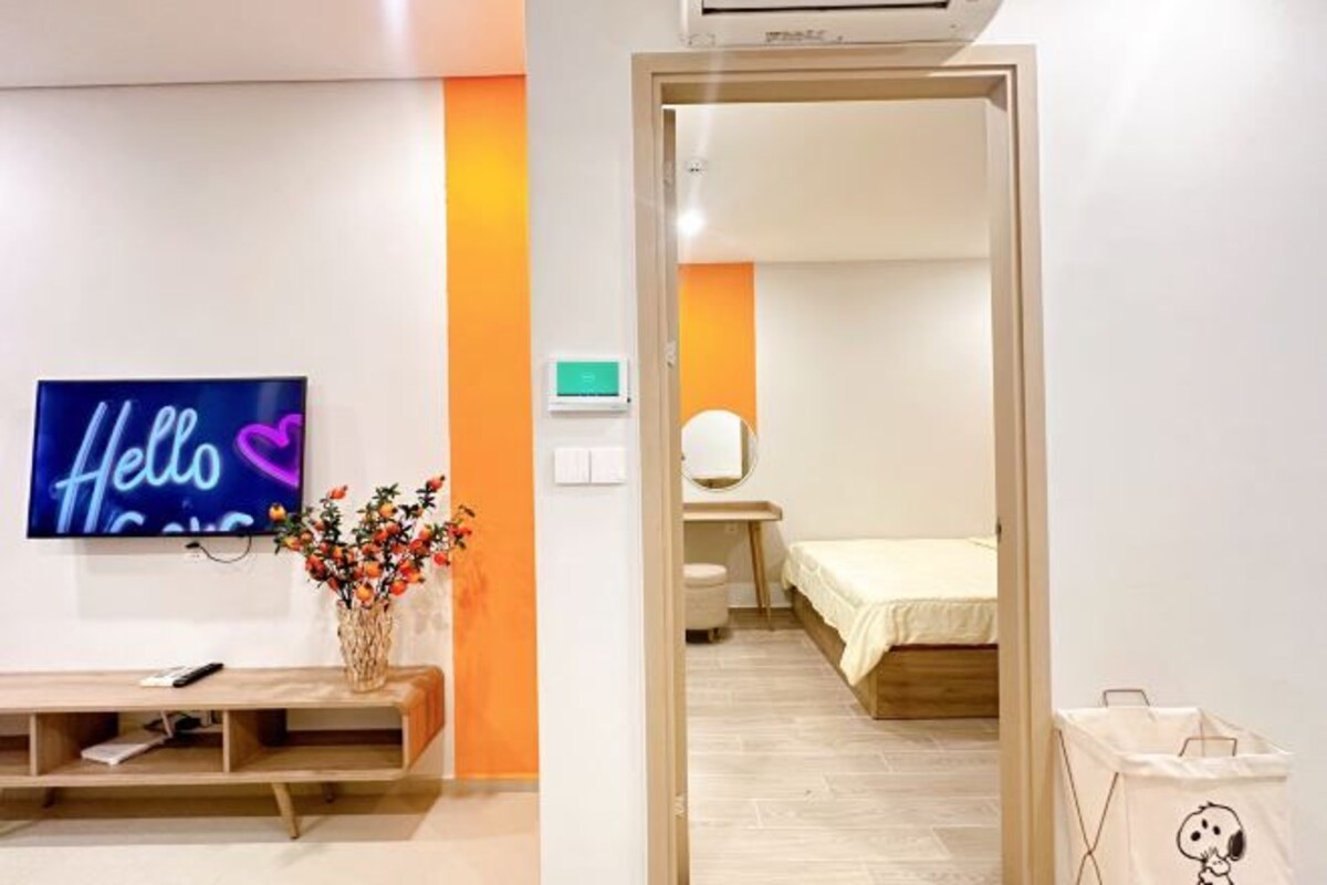 A modern hotel room with a TV, a bedside table, a bed, and a bathroom visible through an open door.