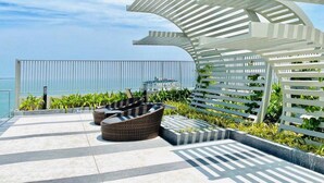 Une terrasse sur le toit, aménagée avec des meubles en osier, une pergola blanche et offrant une vue sur la mer.