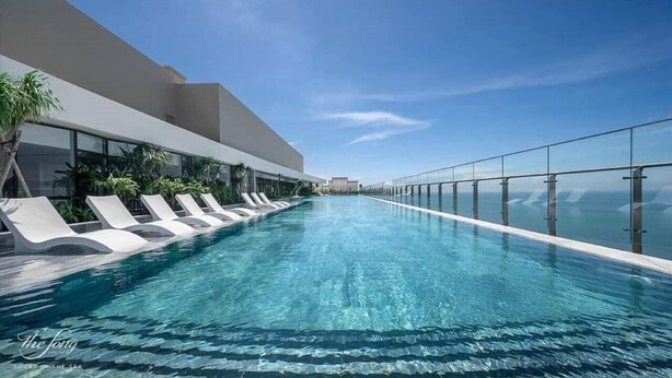 Une piscine à débordement moderne, avec une eau d’un bleu cristallin, entourée de chaises longues et de palmiers, offrant une vue panoramique.