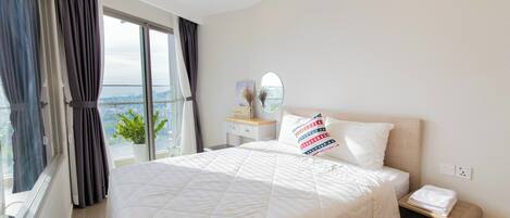 A hotel room with a large bed, a bedside table, a nightstand, a window with curtains, and a view of the city.